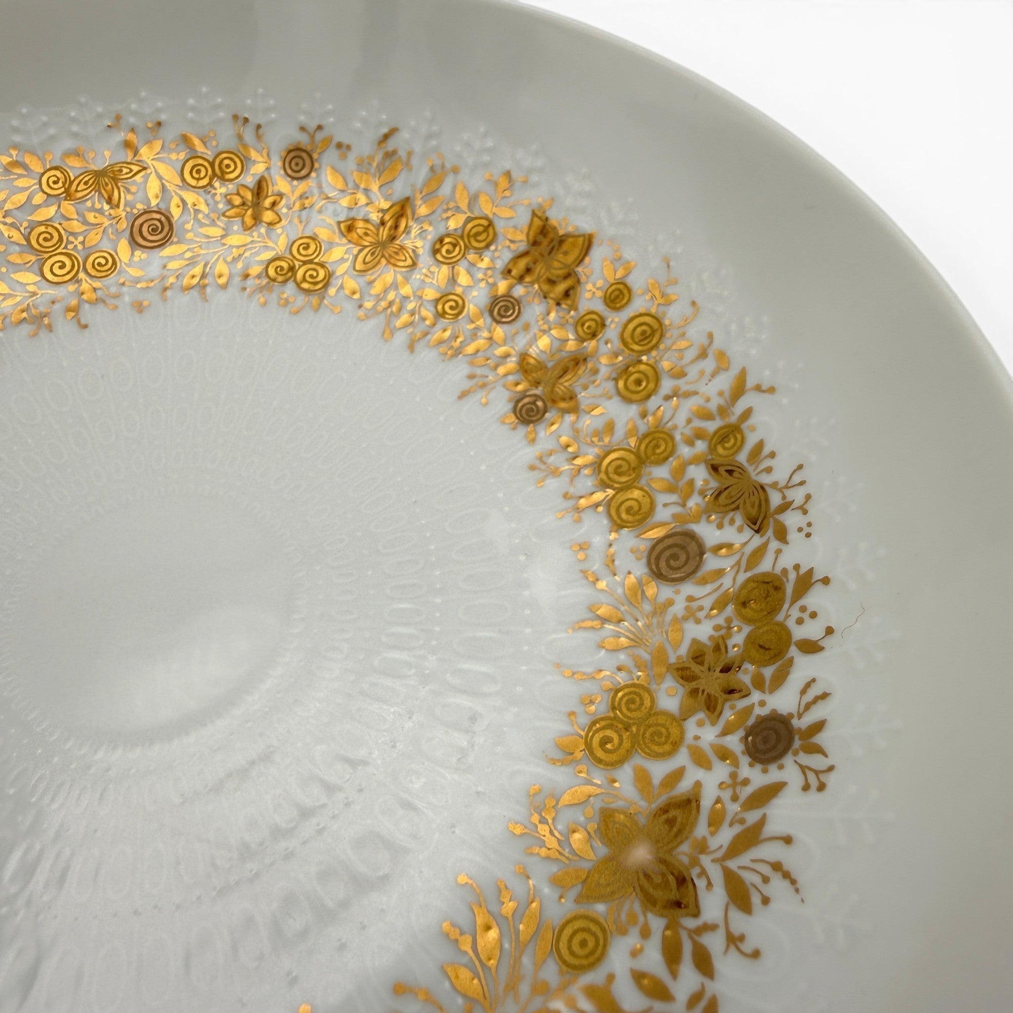 Showroom Ansbach Porzellanteller in Weiß mit filigranem goldenem Blumenmuster und geprägter Textur am Rand.