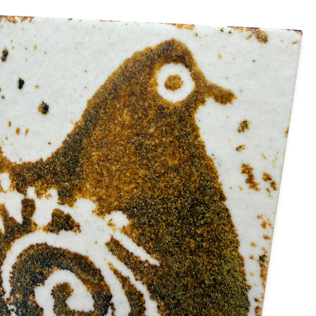 Handgefertigte Showroom Ansbach Keramikfliese mit braunem Vogelmotiv auf cremeweißem, texturiertem Untergrund.